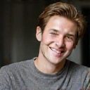 Ritratto professionale di un uomo sorridente, capelli chiari, maglione elegante